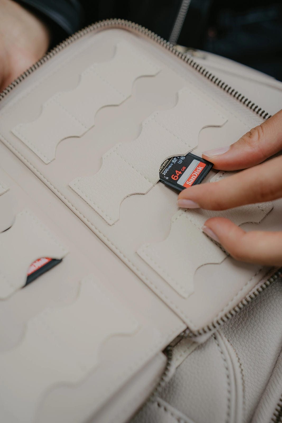 Hand holding a memory card over an open beige leather wallet.