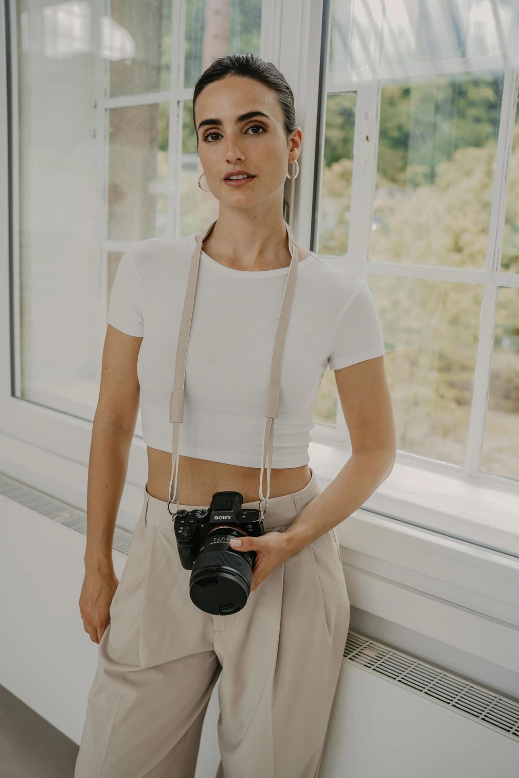 Woman holding a camera indoors with large windows in the background