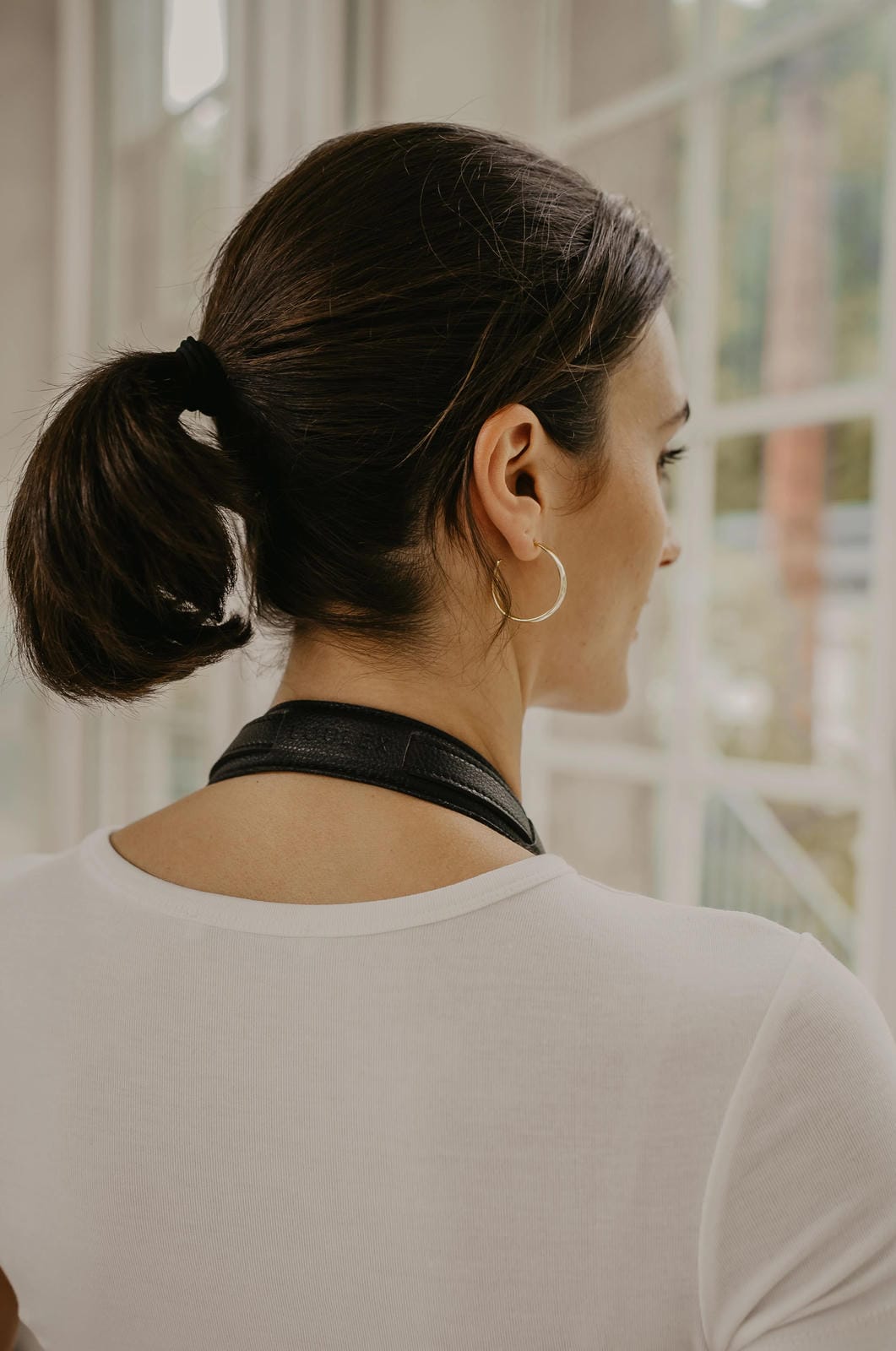 Femme avec une queue de cheval portant un collier ras-du-cou noir devant une fenêtre.