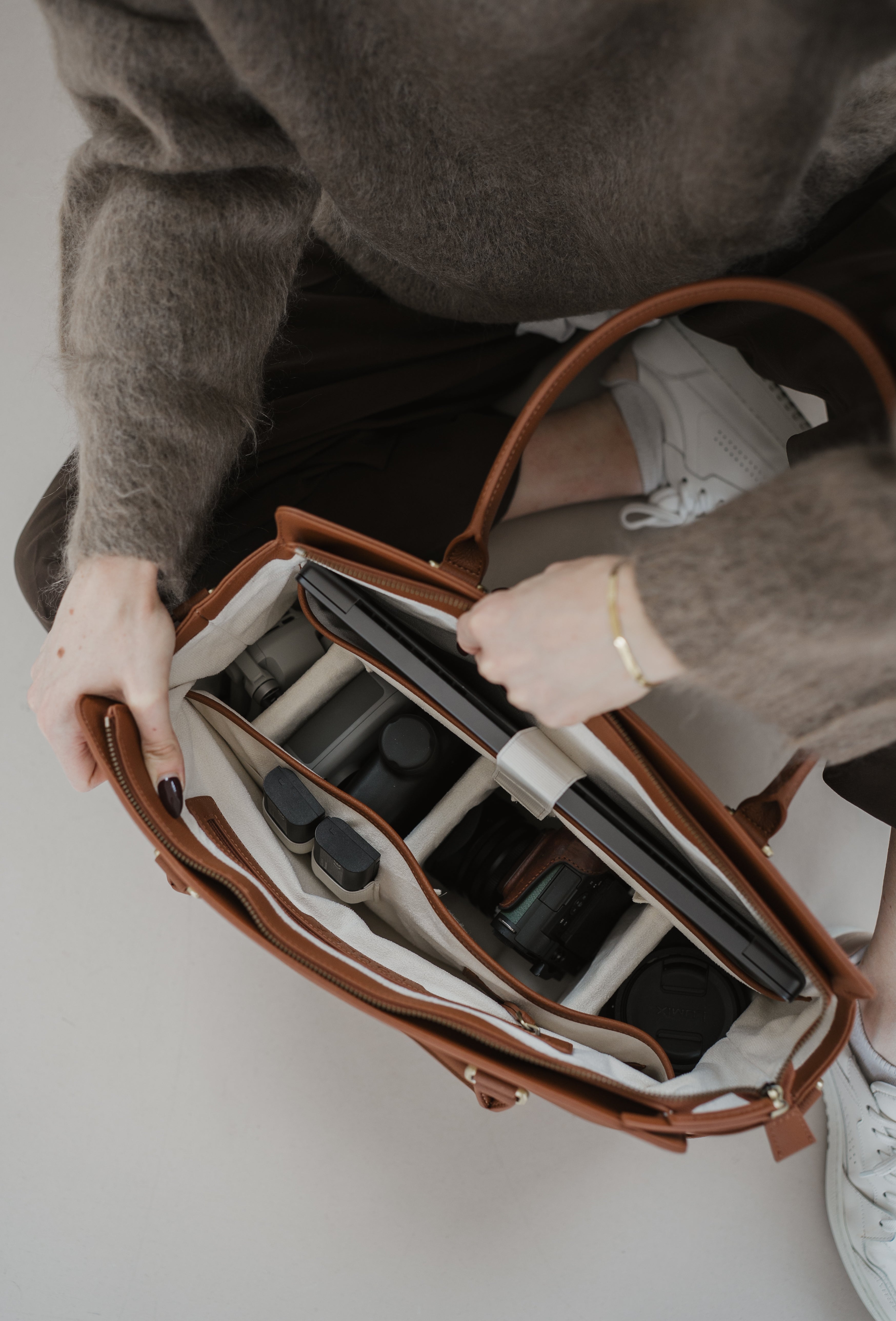 Person opening a brown leather bag with compartments on a light background