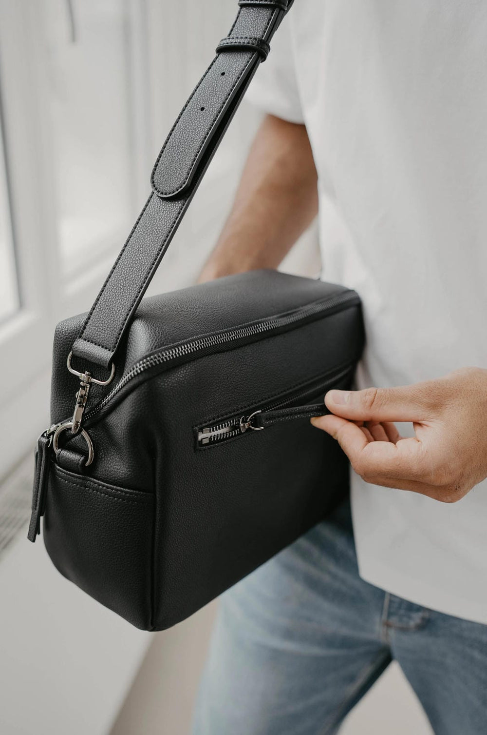 Persona con un bolso bandolera negro y fondo difuminado.