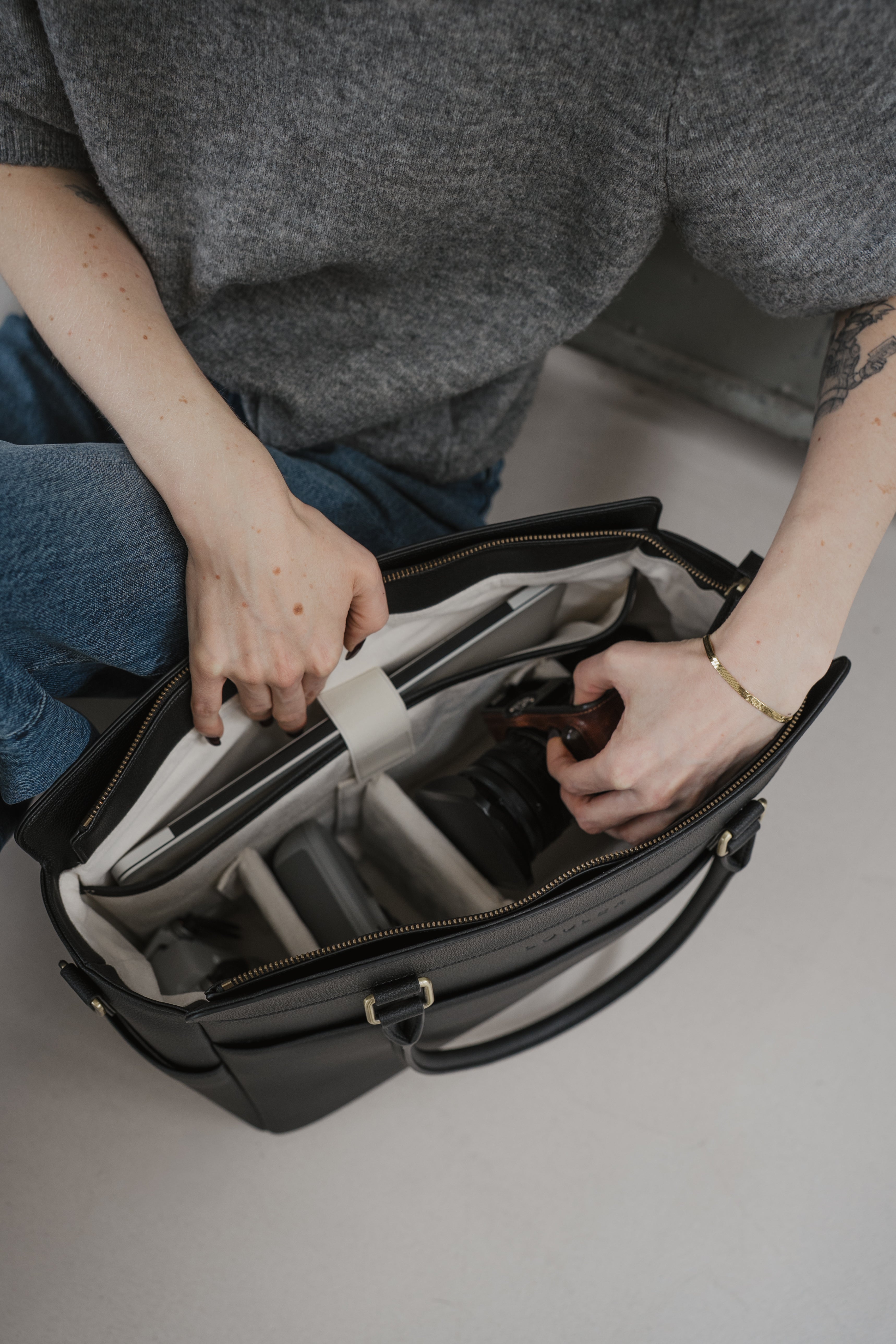 Person organizing a black bag with compartments on a light gray surface