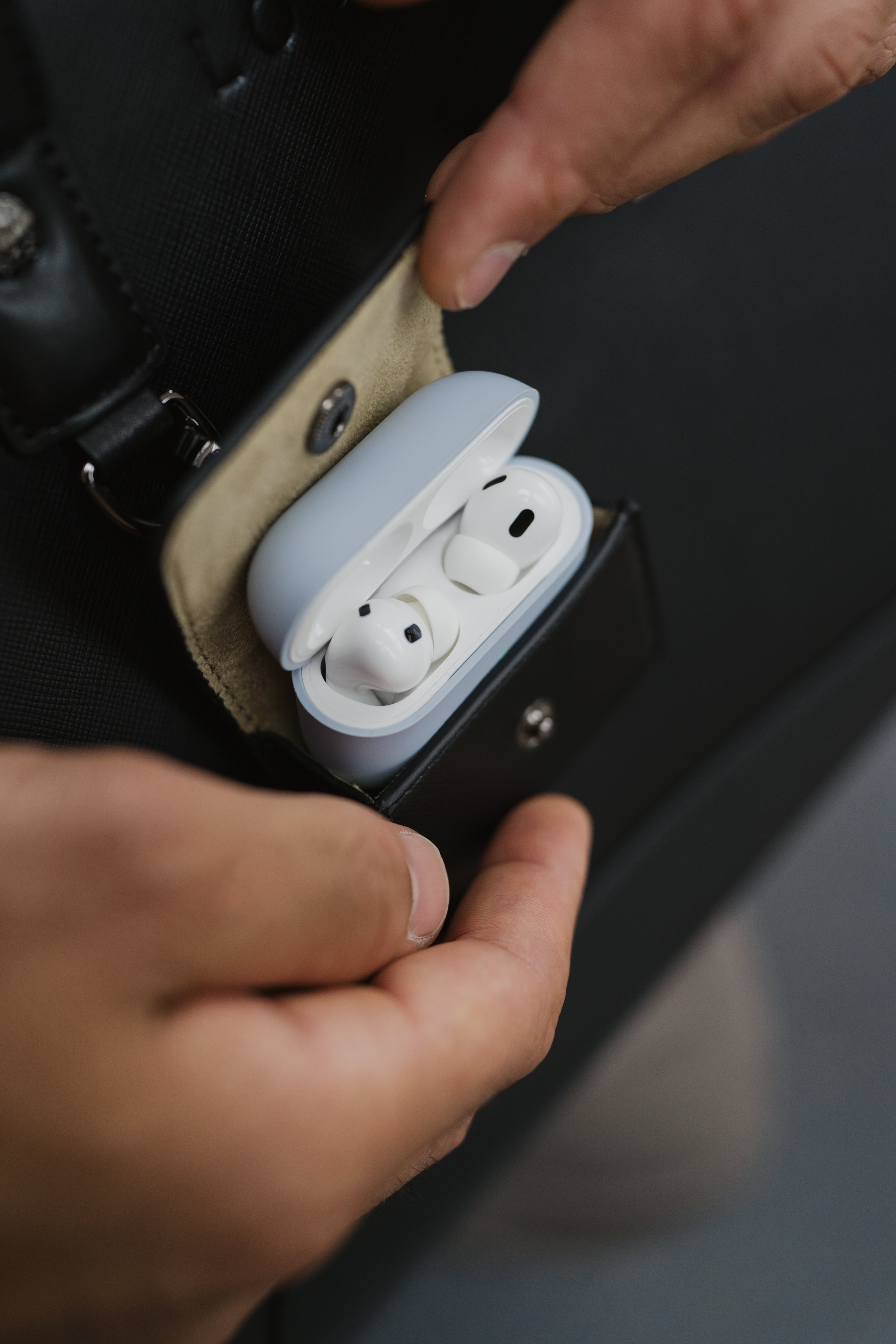 White wireless earbuds in a black case held by a person's hand.