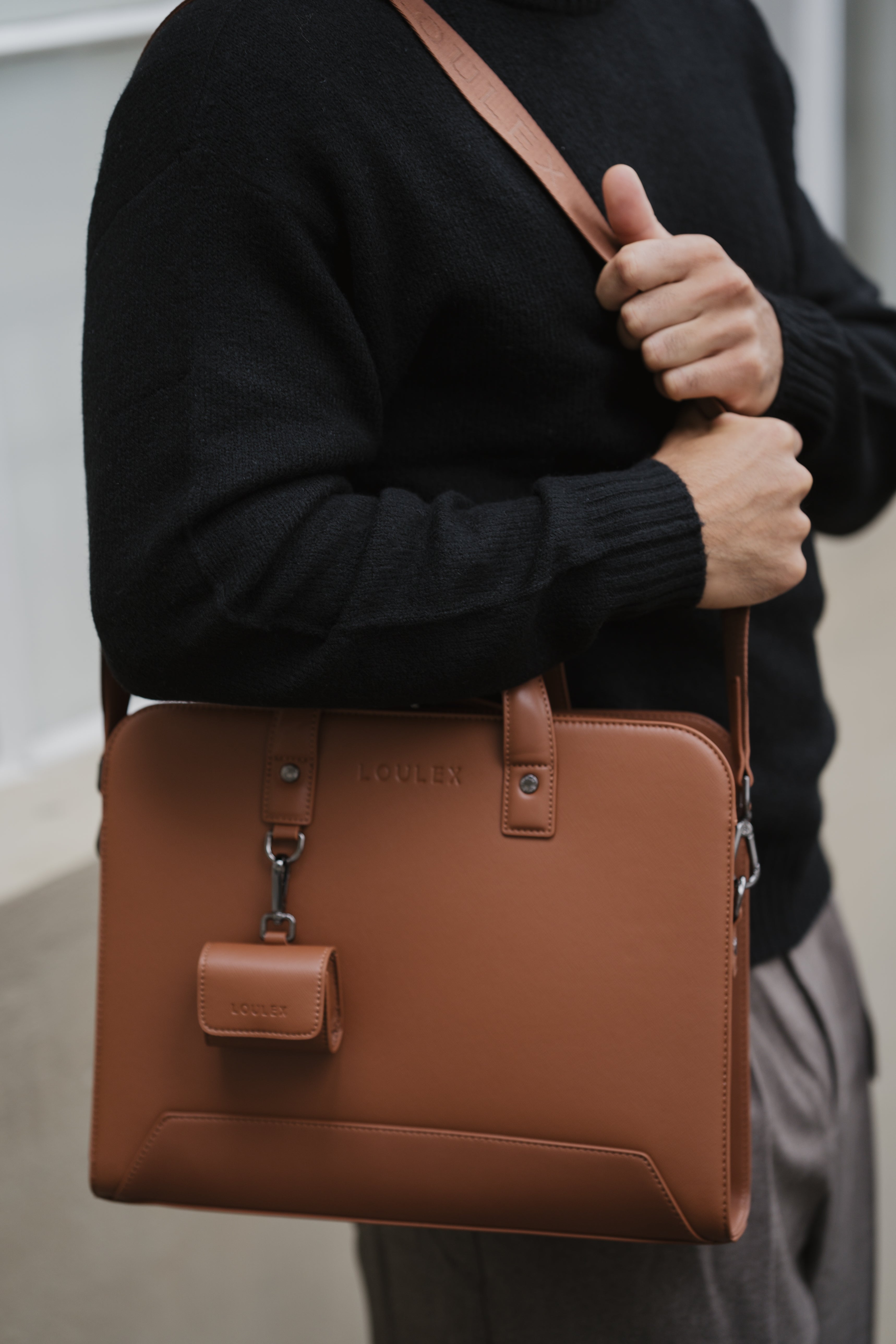 Person holding a brown leather bag with a visible brand logo.