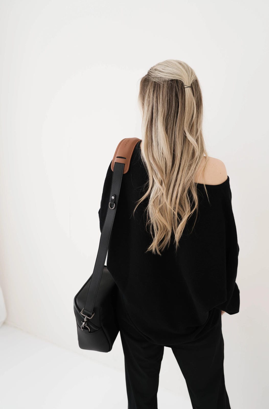 Person wearing a black off-shoulder top and carrying a black bag on a white background