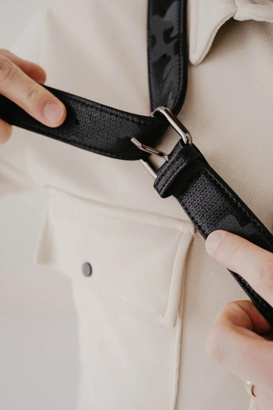 Person adjusting a black strap on a beige garment