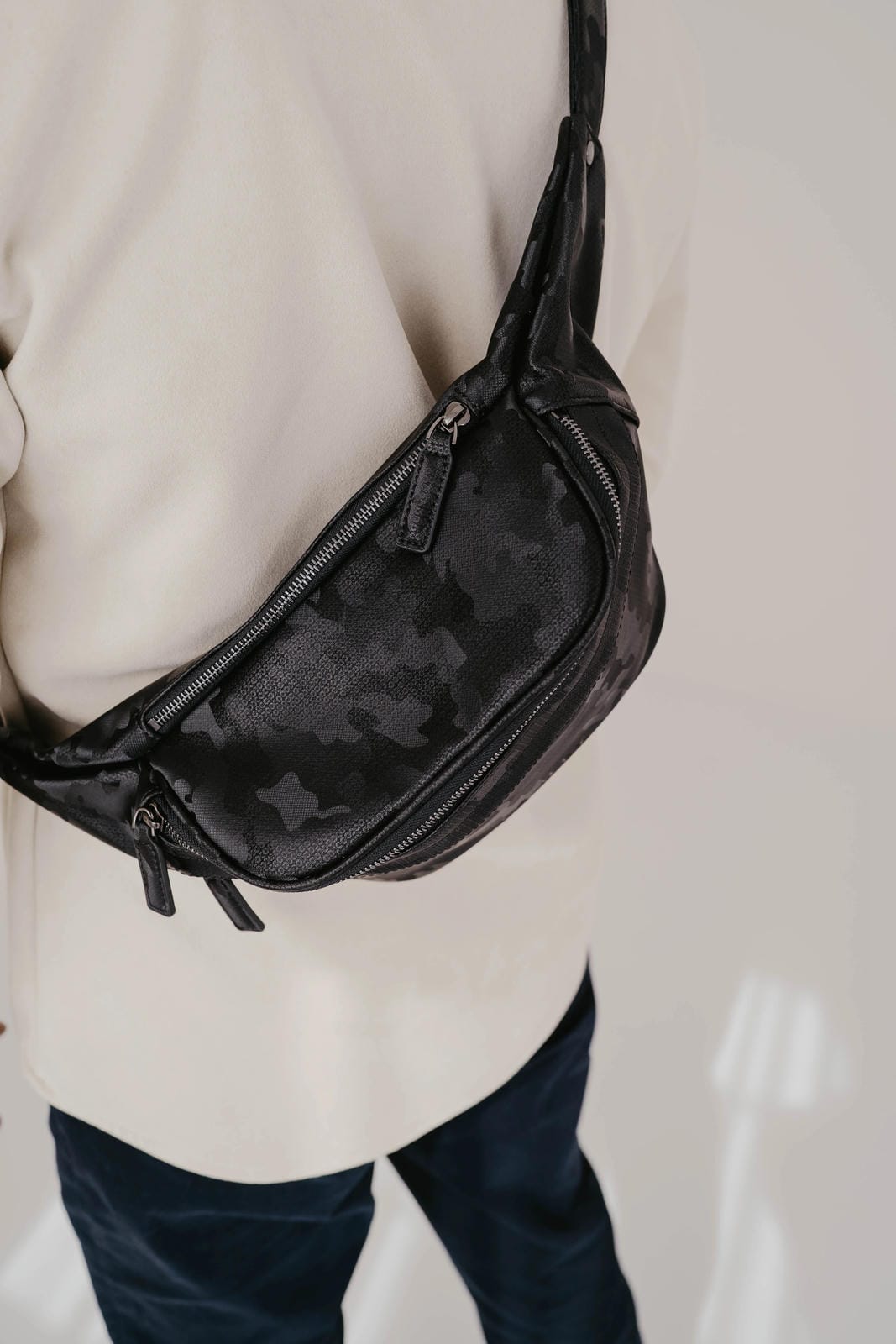 Person wearing a black camouflage-patterned bag over their shoulder against a neutral background