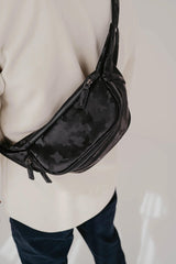 Persona con una borsa nera con motivo mimetico a tracolla su uno sfondo neutro