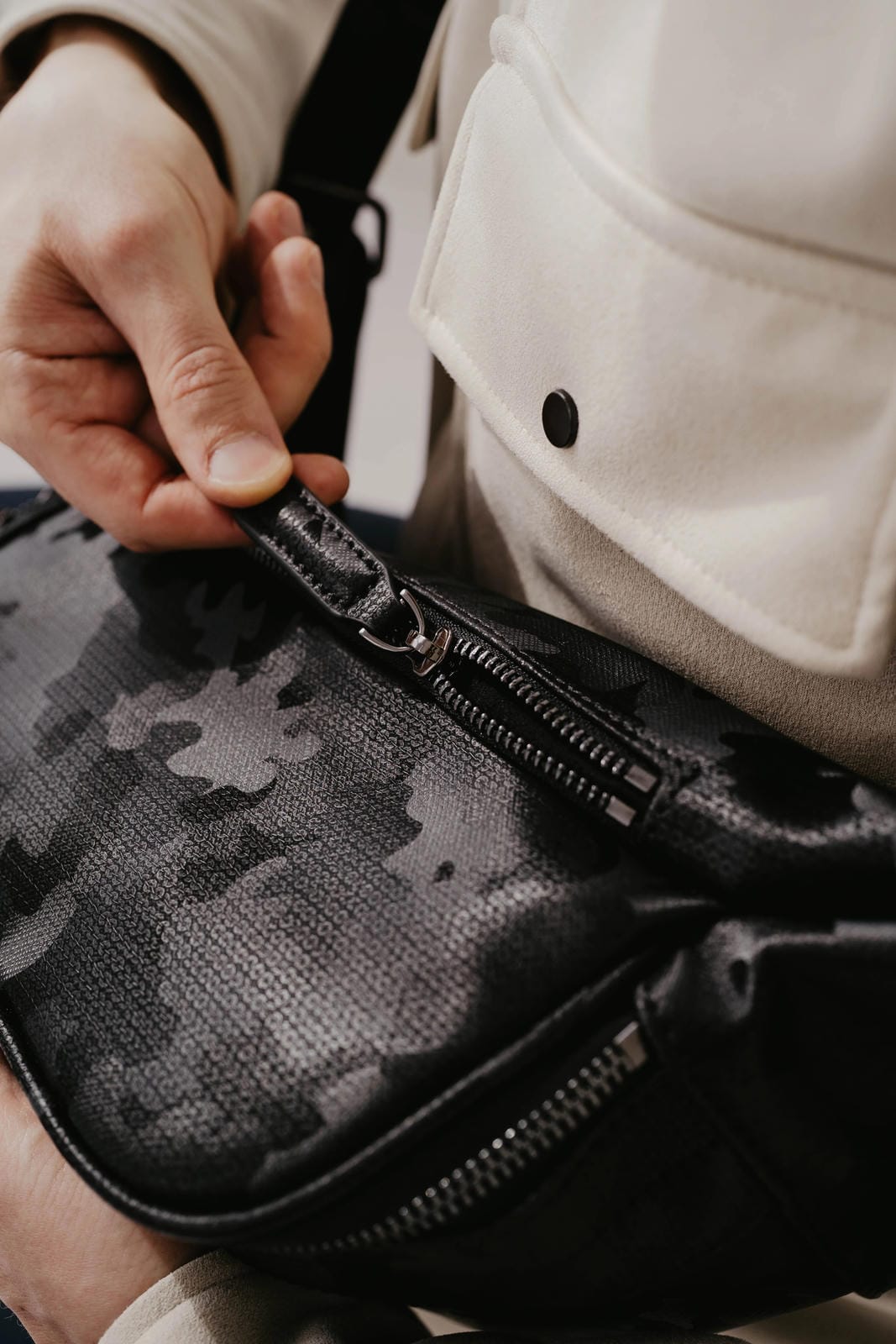 Person opening a camouflage-patterned bag with a neutral background