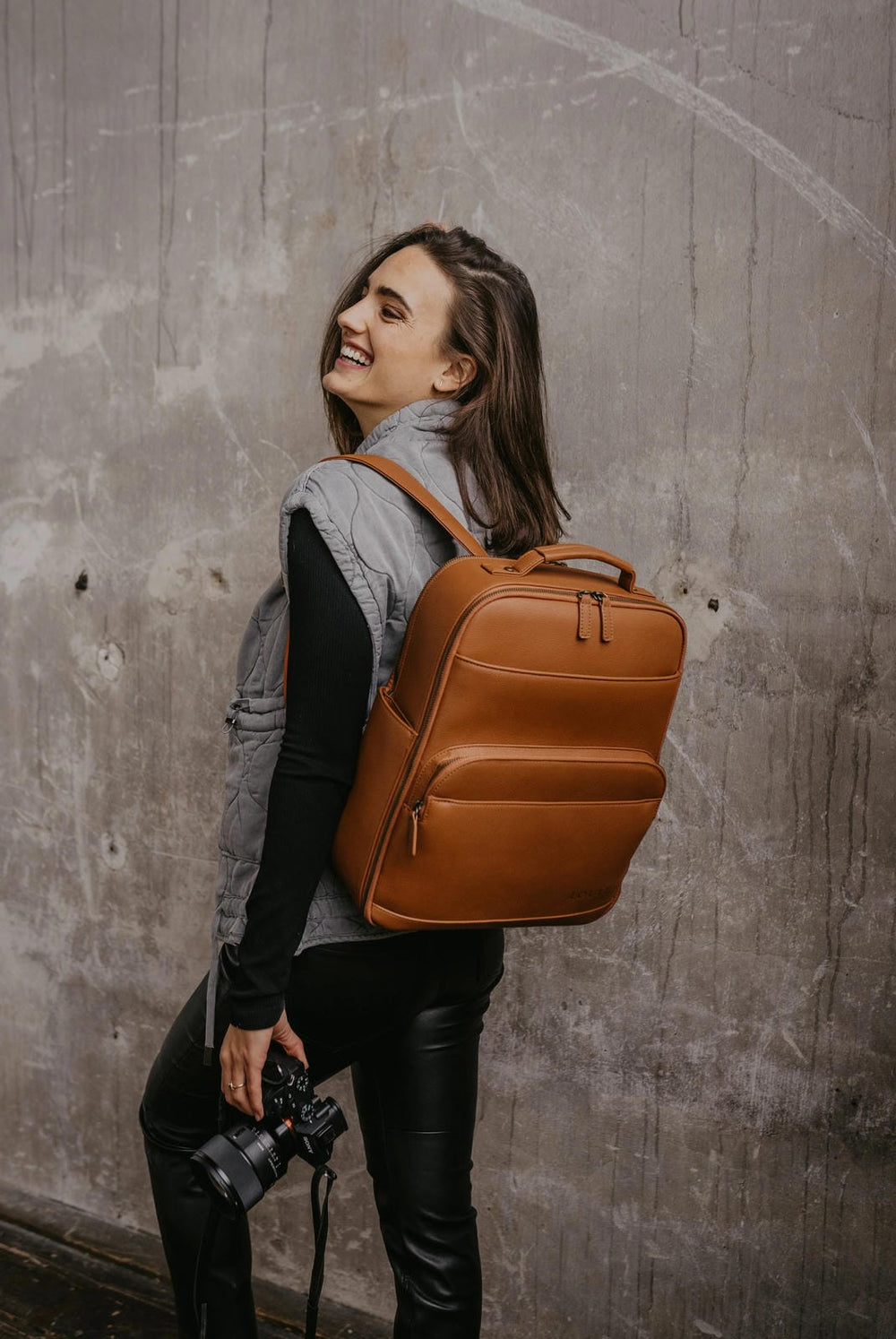 Mujer con una mochila marrón frente a una pared con textura