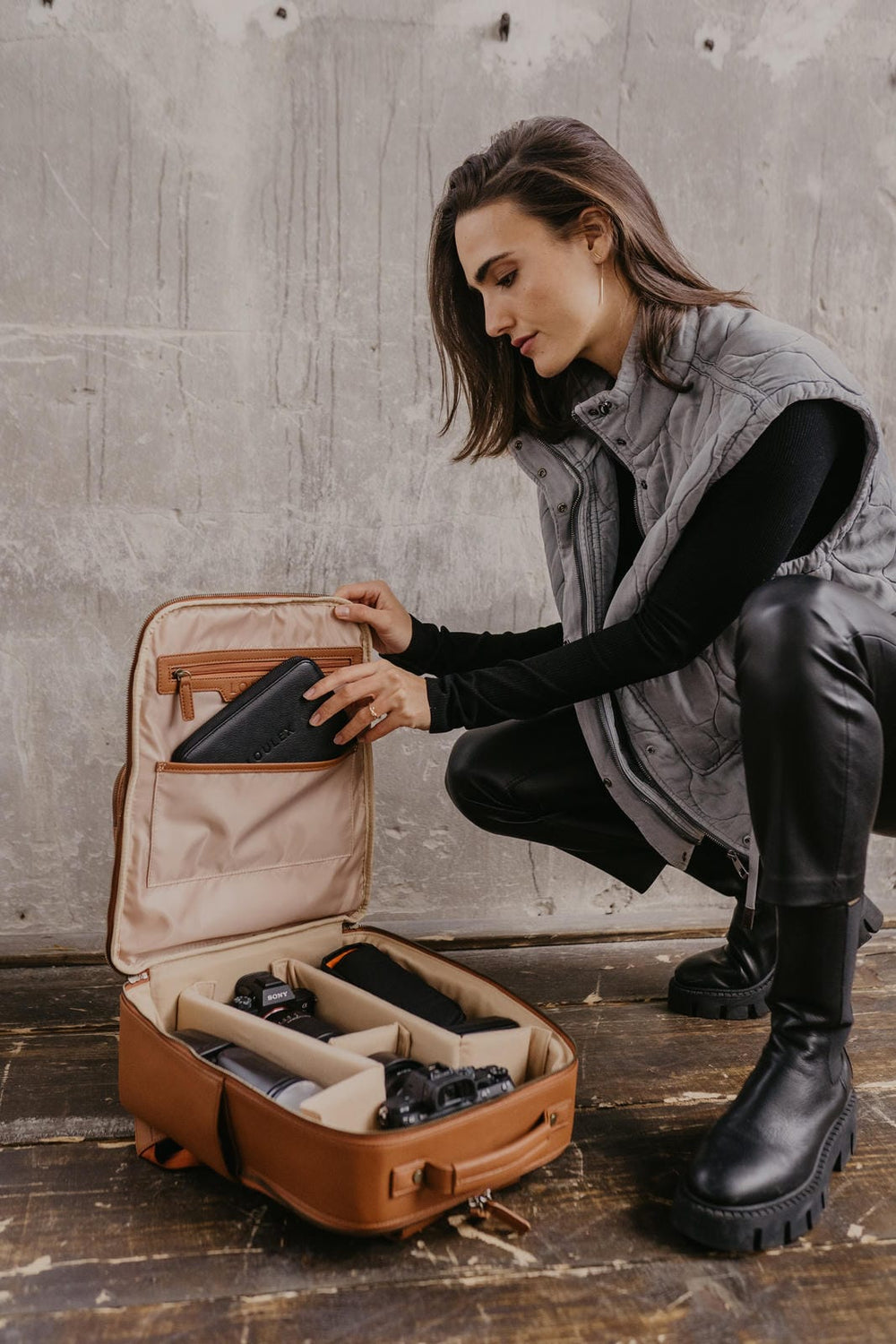 Mujer organizando una maleta marrón con compartimentos sobre un suelo de madera.