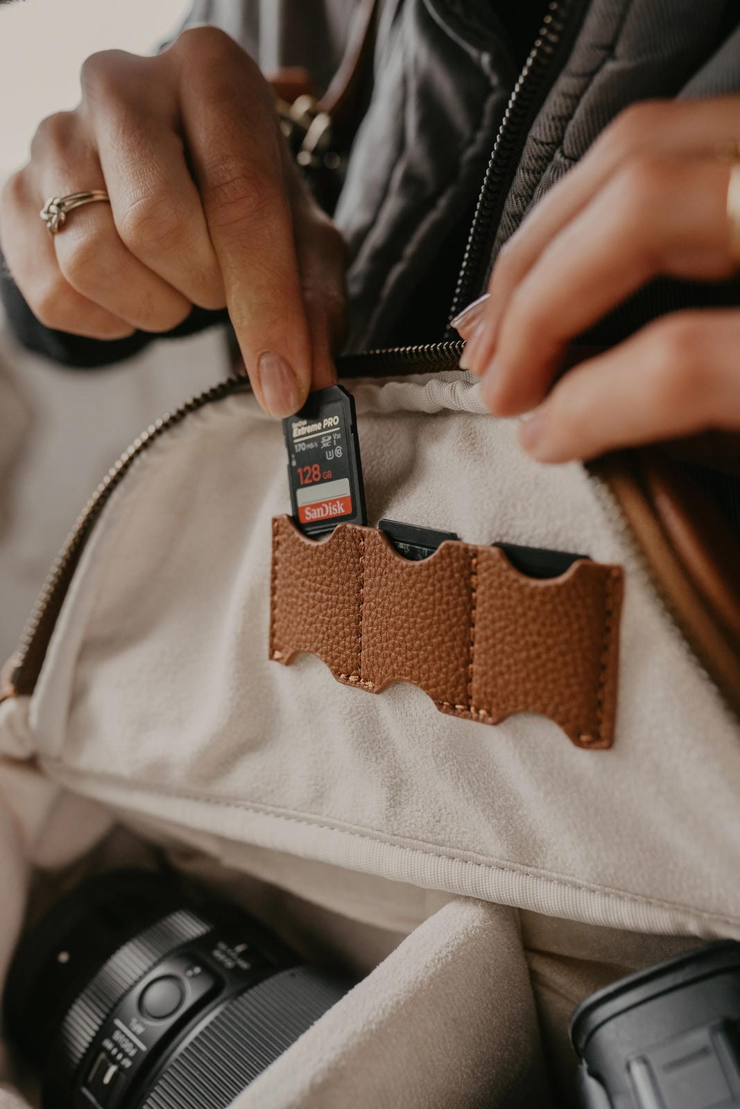 Person holding an SD card near a camera in a beige jacket with a brown pocket.
