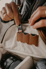 Persona che tiene una scheda SD vicino a una fotocamera, con una giacca beige con tasche marroni.