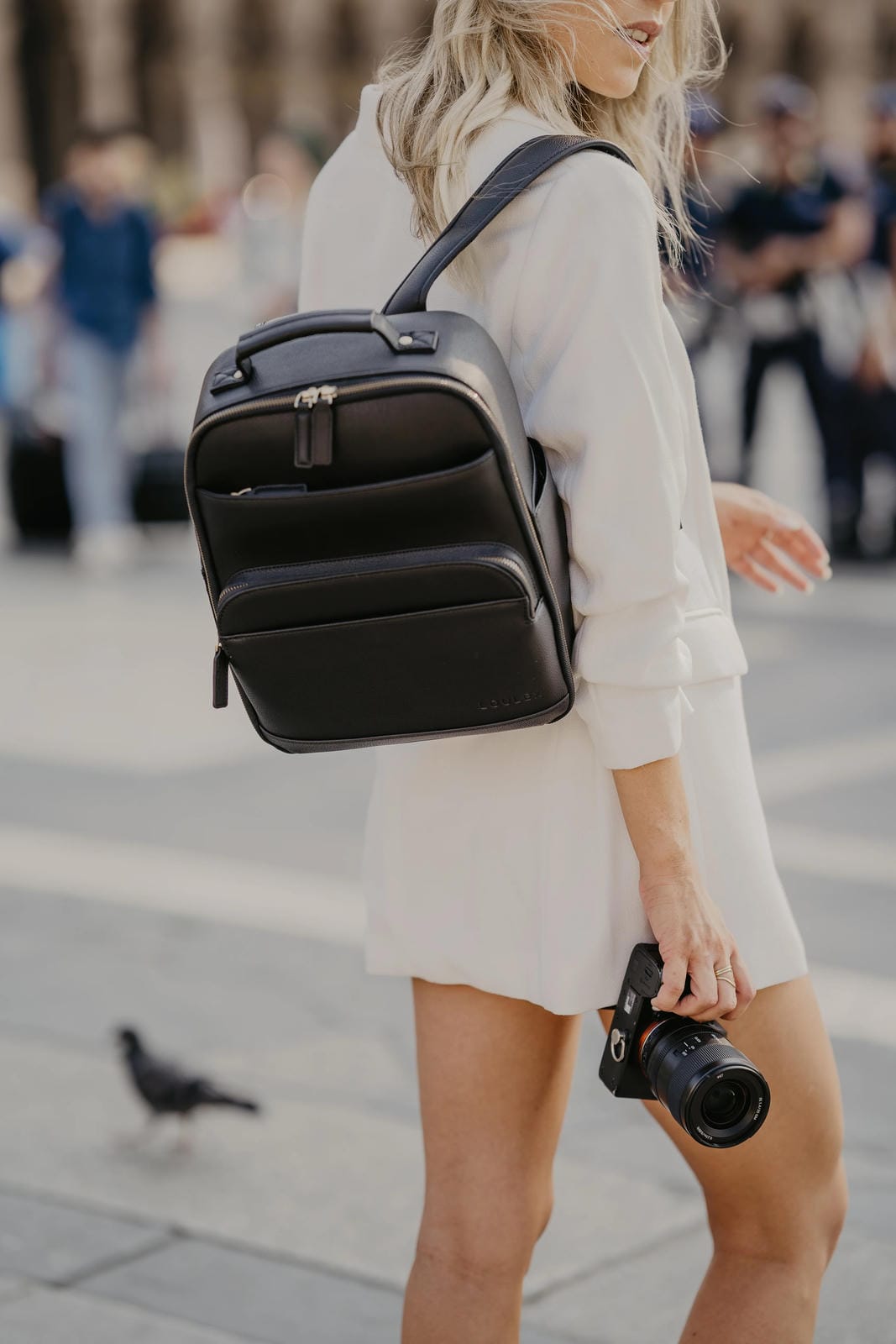 Person wearing a black backpack and holding a camera on a city street.