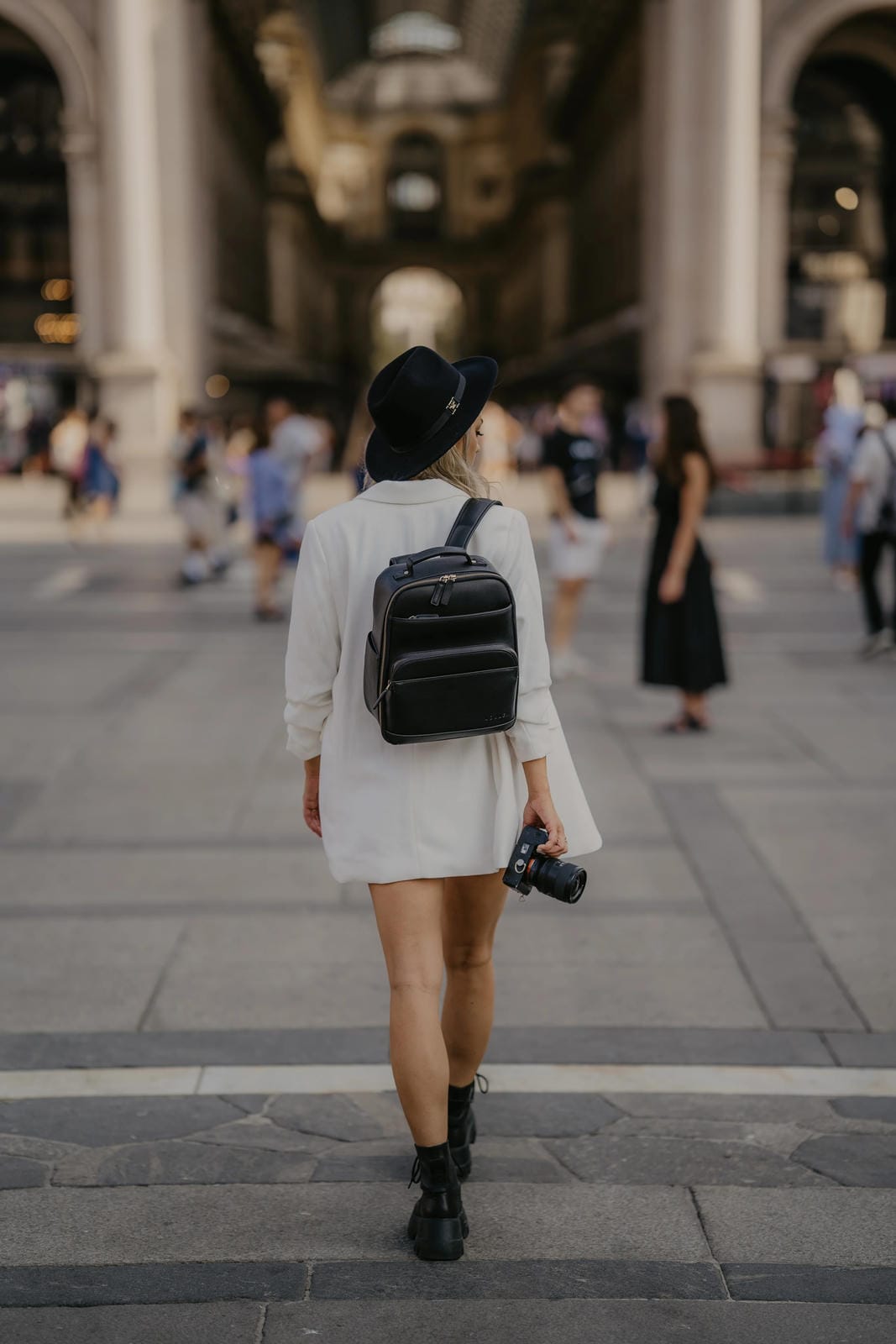 Person walking in an urban setting with a black backpack and camera