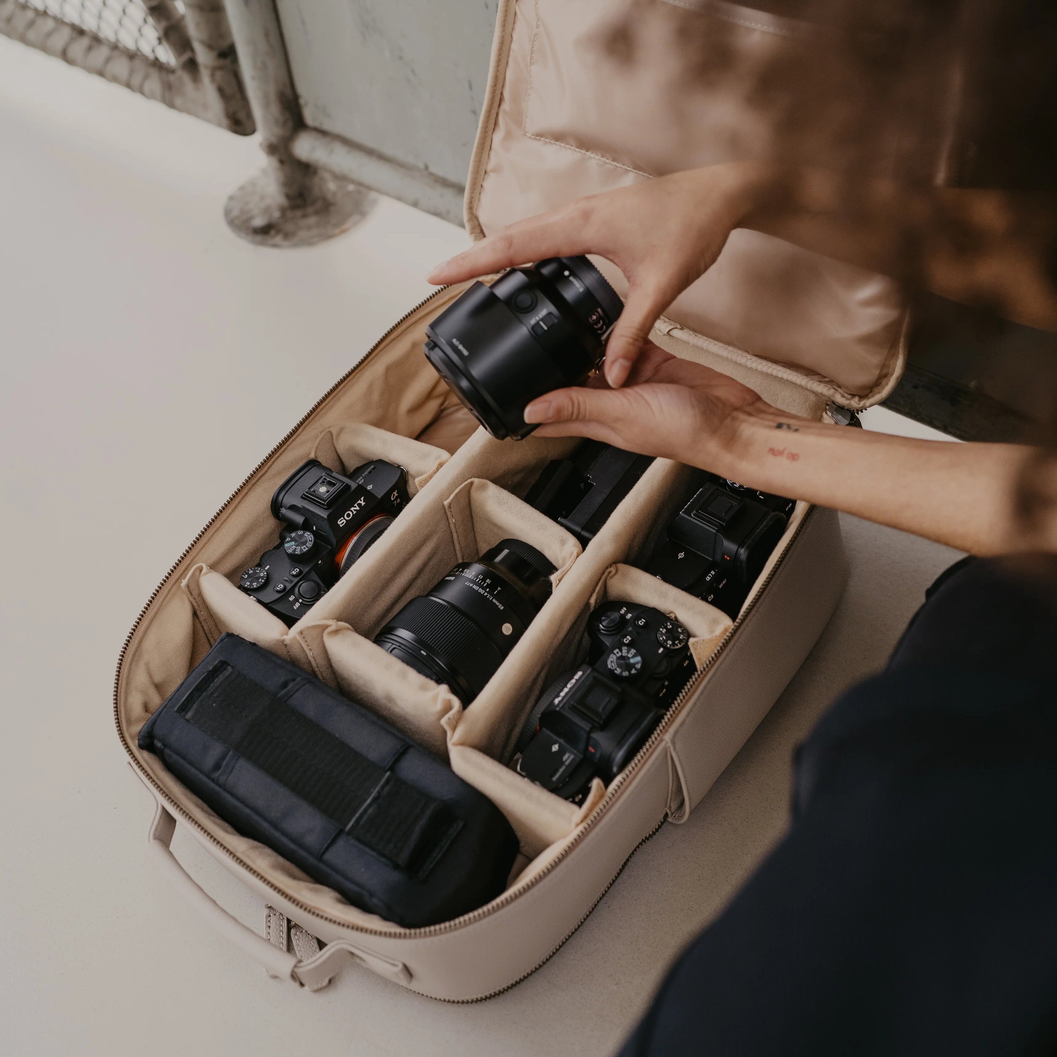 Person organizing cameras in a beige travel bag.