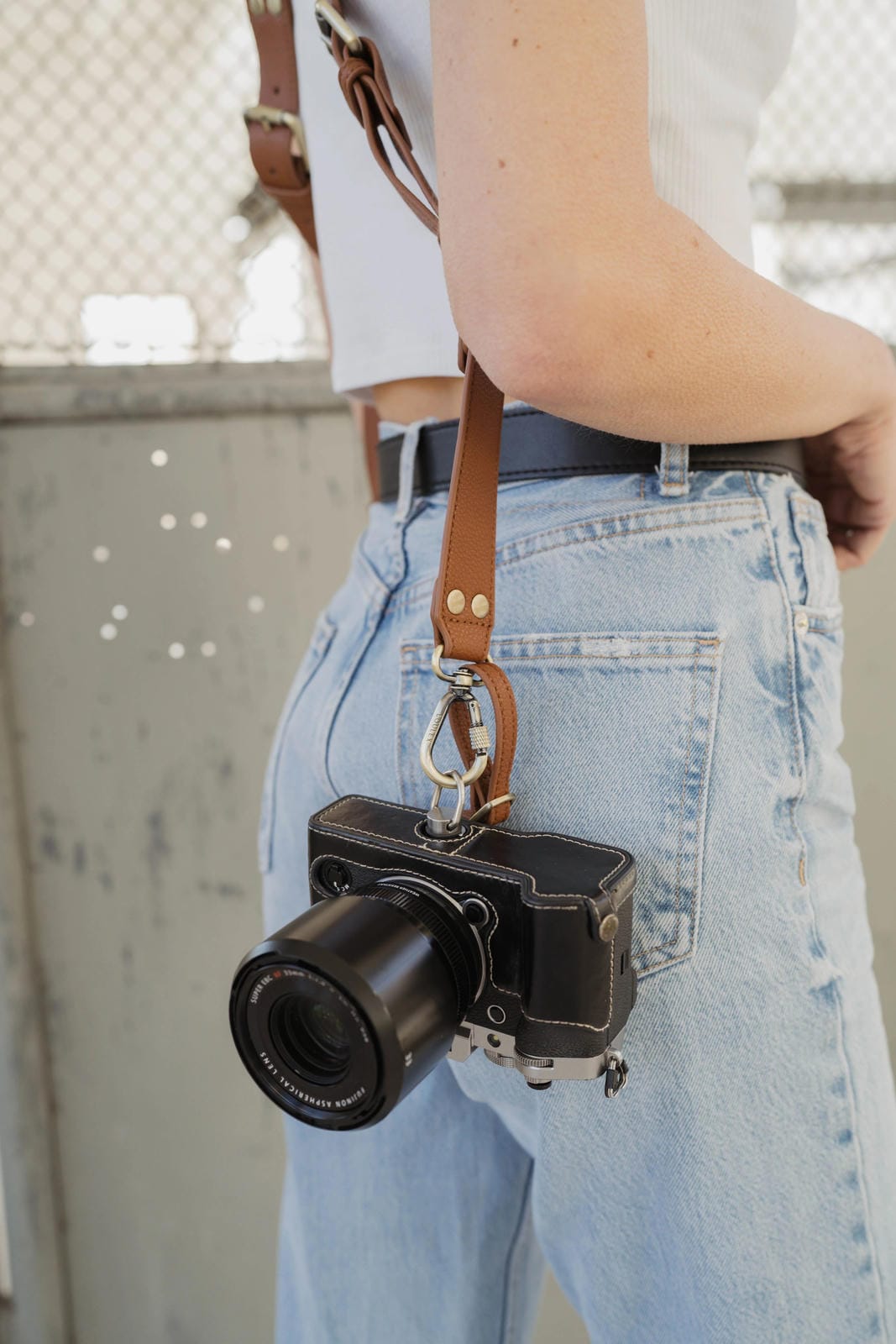 Person holding a black camera with a leather strap against a neutral background