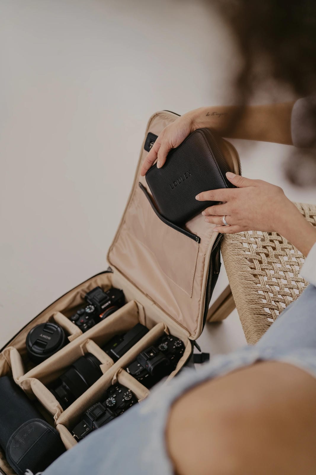 Person organizing camera equipment in a beige travel case.