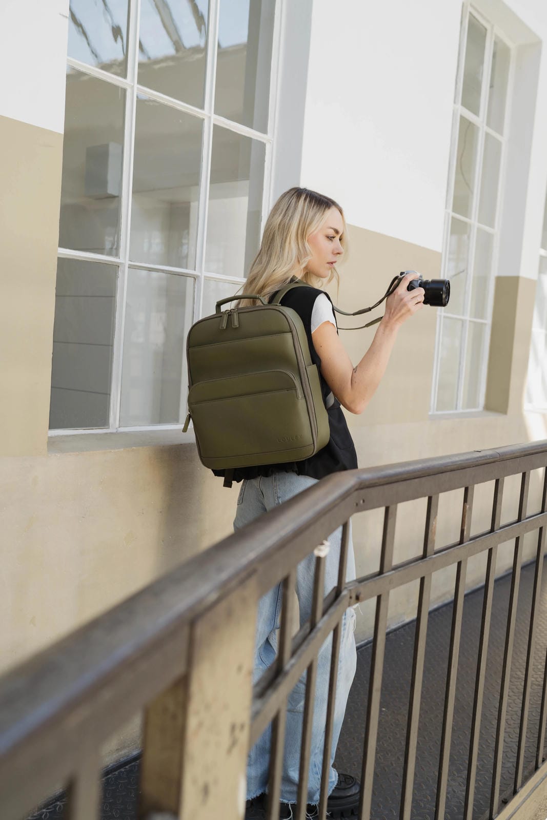 Person with a green backpack holding a camera, standing on a balcony.