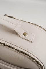 Zbliżenie na beżową skórzaną torbę z zamkiem błyskawicznym i złotym guzikiem.