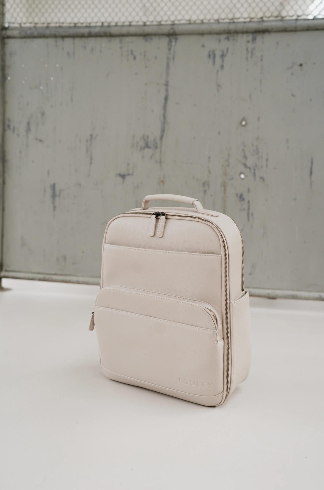 Beige backpack on a light gray surface with a textured wall background