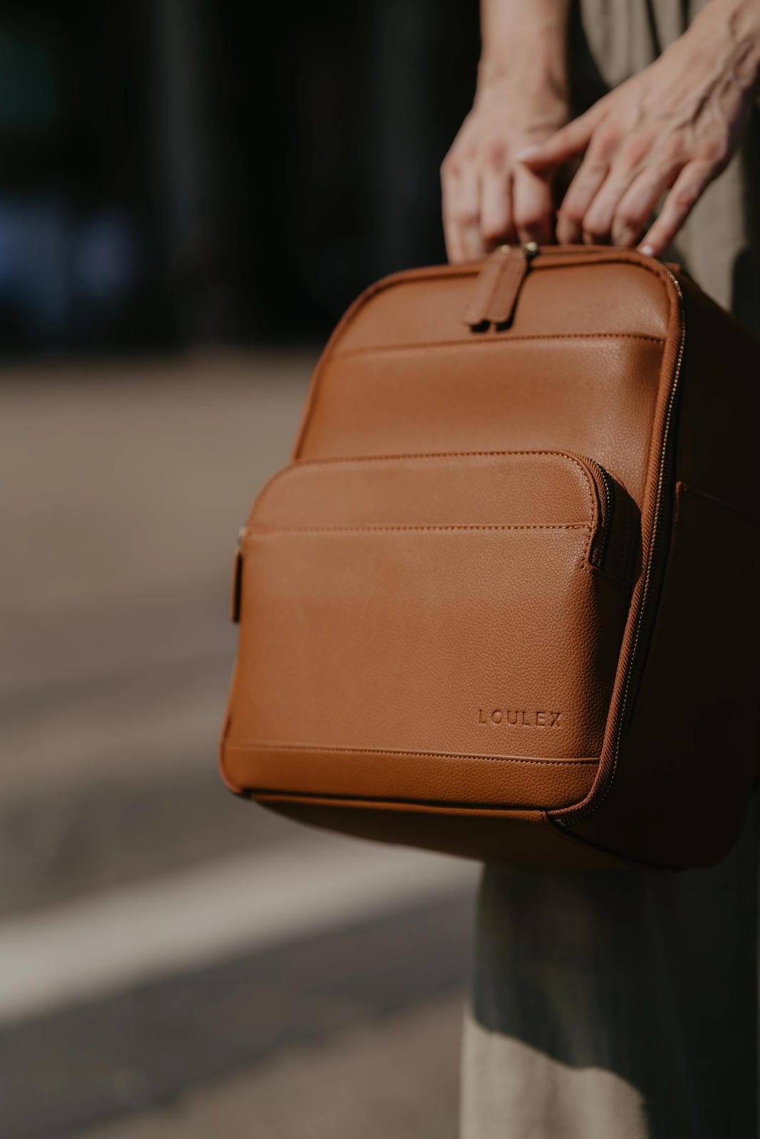 Brown leather backpack held by a person with a blurred background