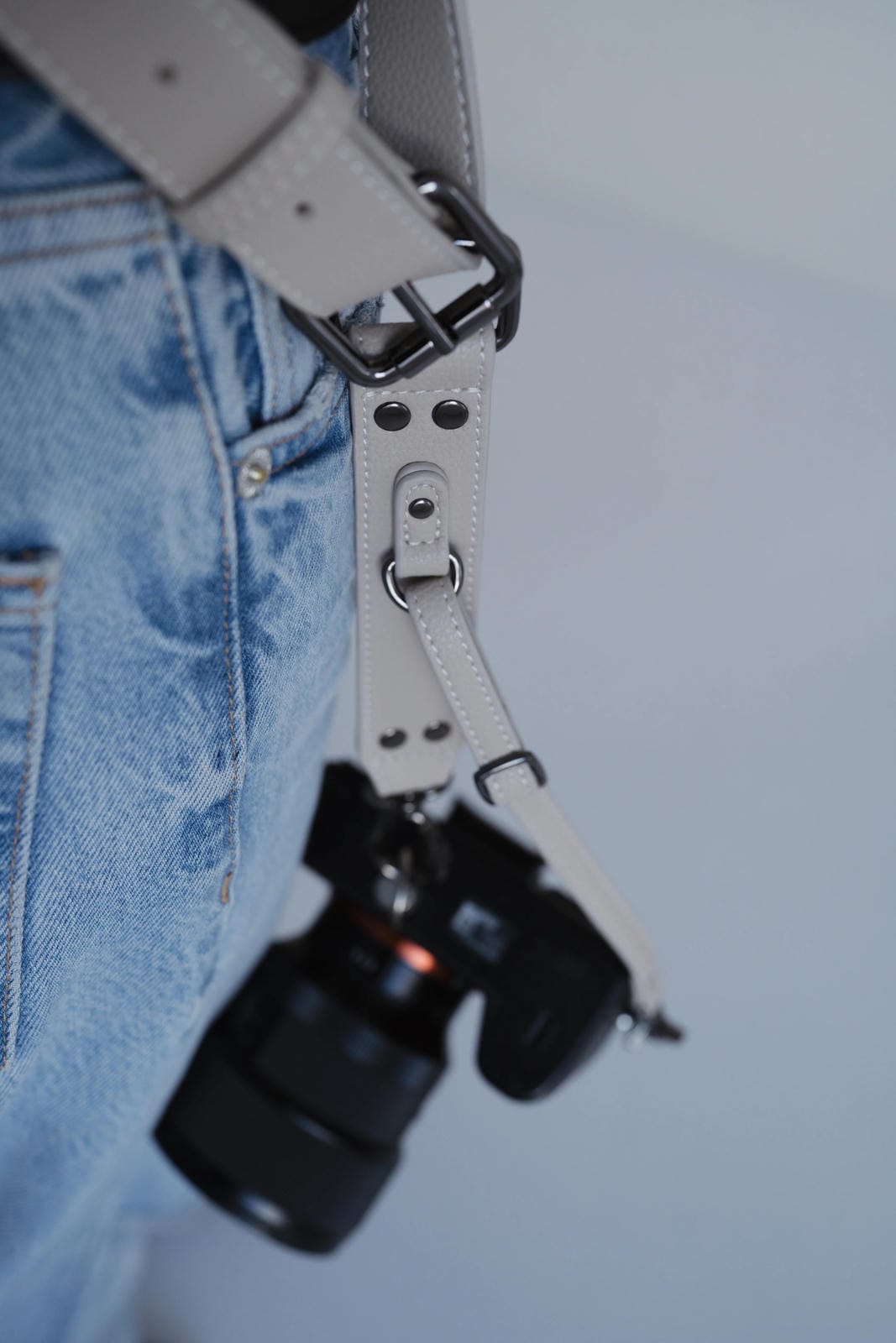 Camera with a strap attached to blue jeans on a plain background