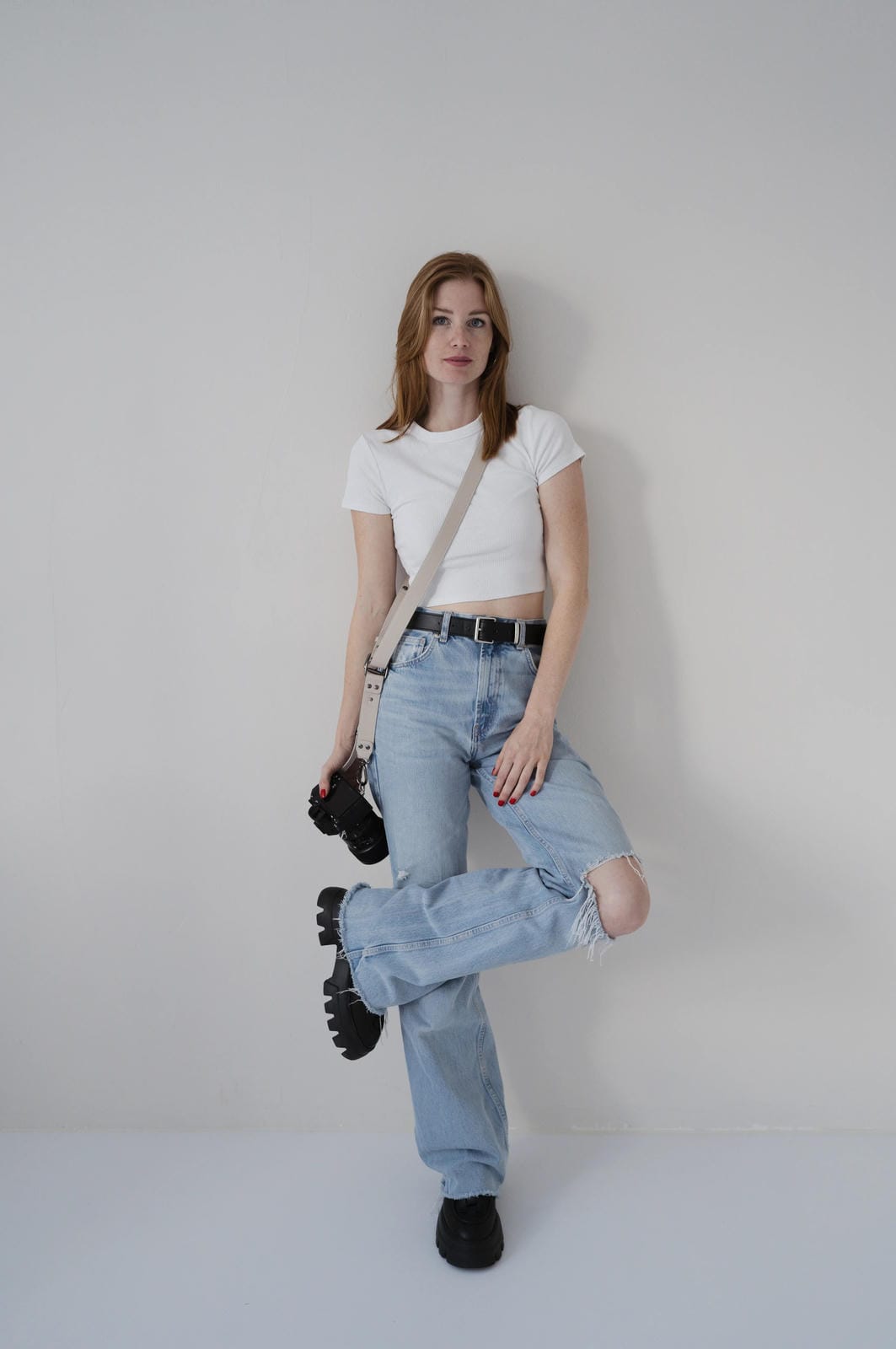 Person wearing a white t-shirt, light blue jeans, and black shoes against a plain background