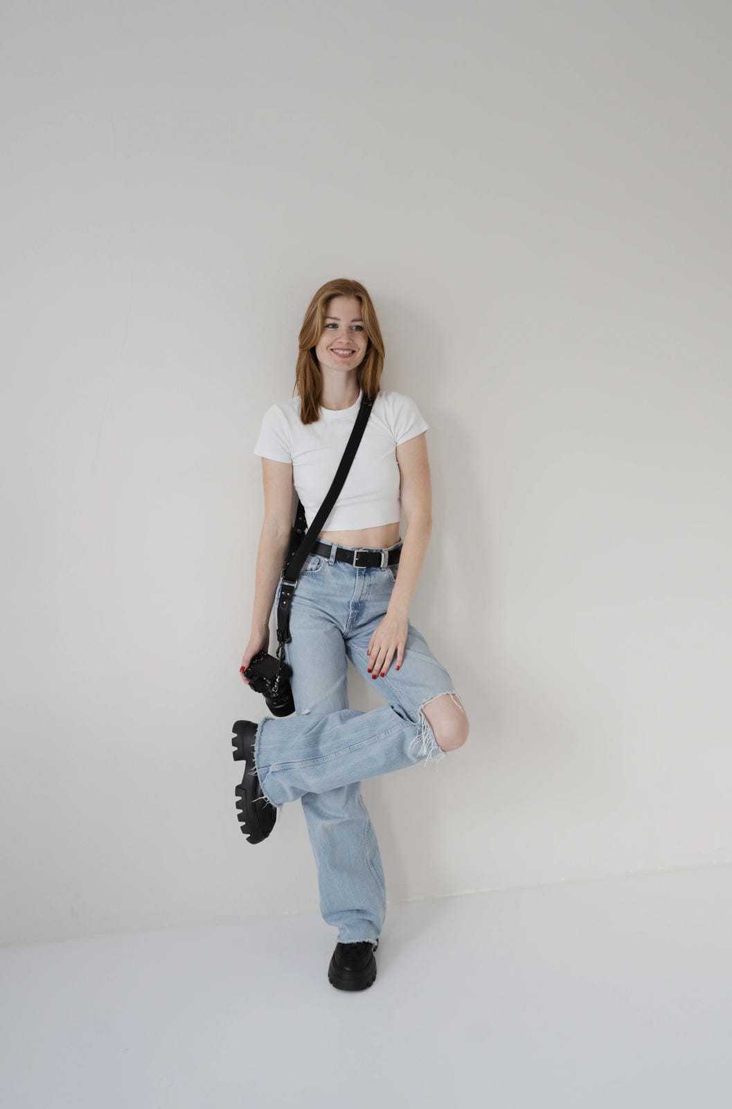Person wearing a white t-shirt, light blue jeans, and black shoes on a plain background