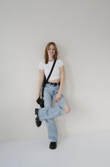 Persoon met een wit T-shirt, lichtblauwe jeans en zwarte schoenen op een effen achtergrond