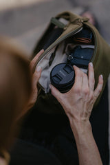 Persona che tiene in mano un obiettivo fotografico Sony accanto a una borsa aperta