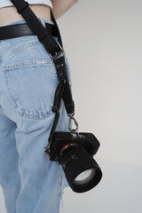 Cameralens bevestigd aan een zwarte riem boven een lichtblauwe spijkerbroek op een effen achtergrond