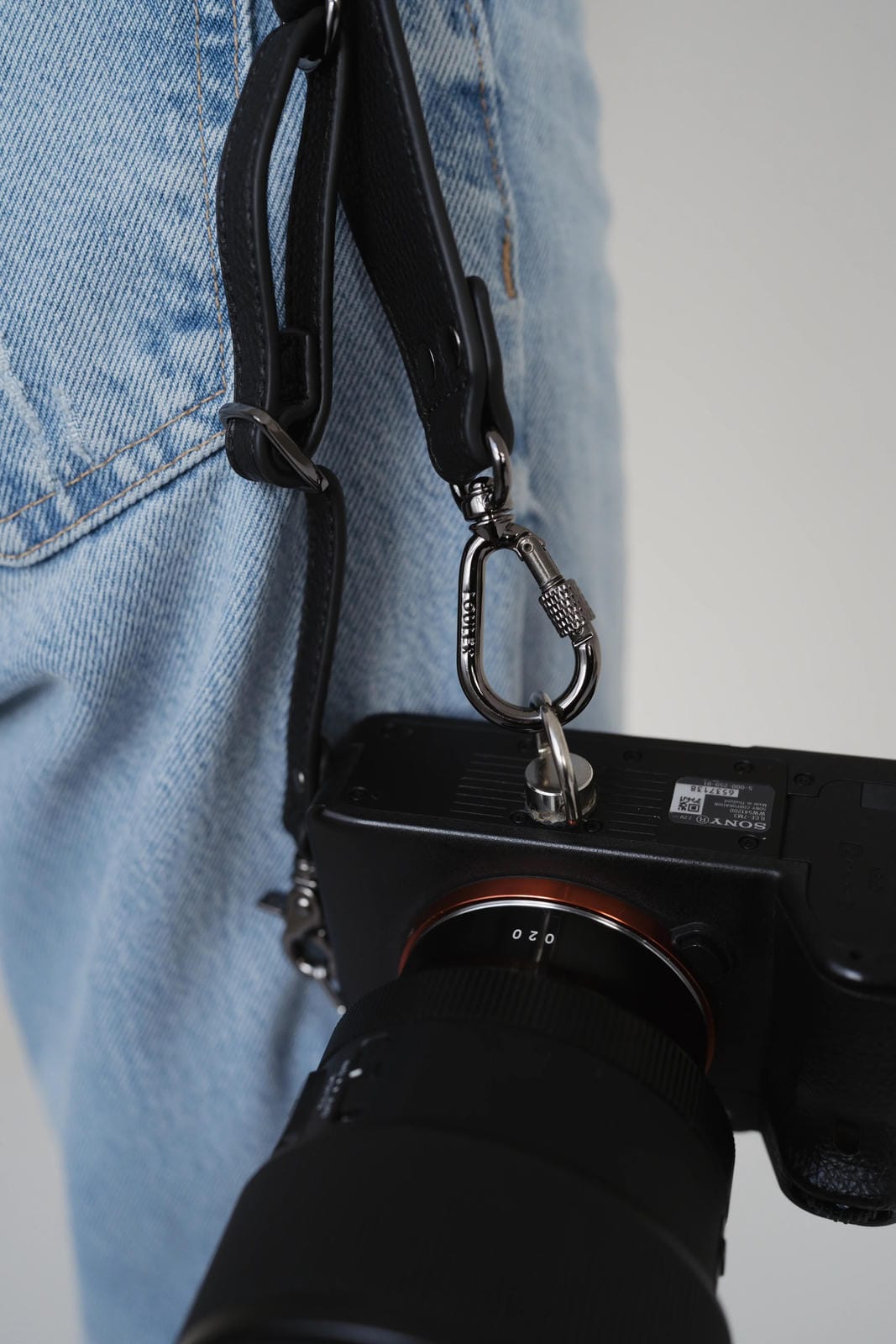 Camera with strap attached to jeans on a plain background