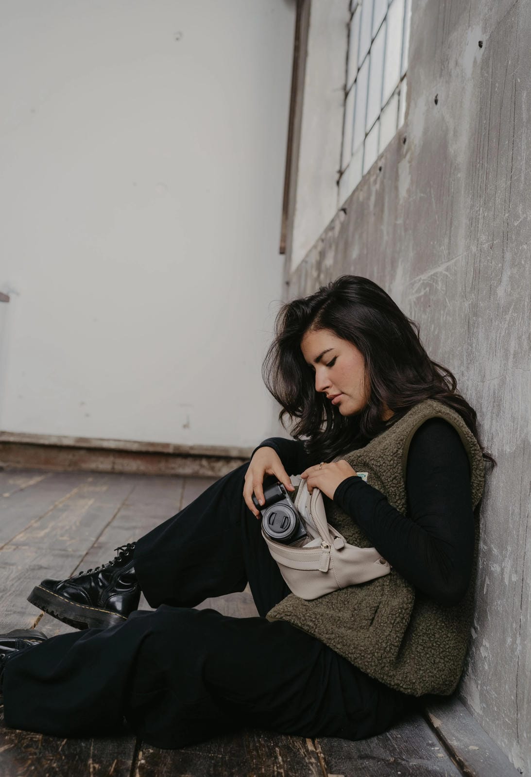 Woman sitting on a step holding a camera, wearing a green vest and black pants.