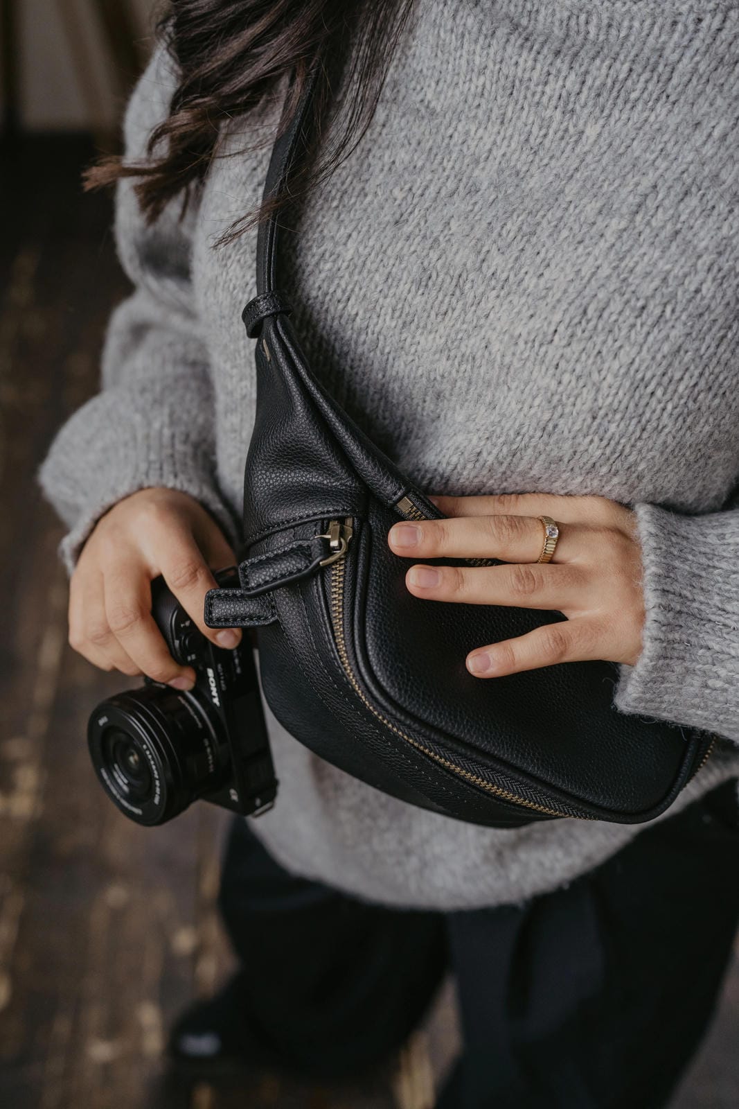 Person holding a black camera and black waist bag with a blurred background