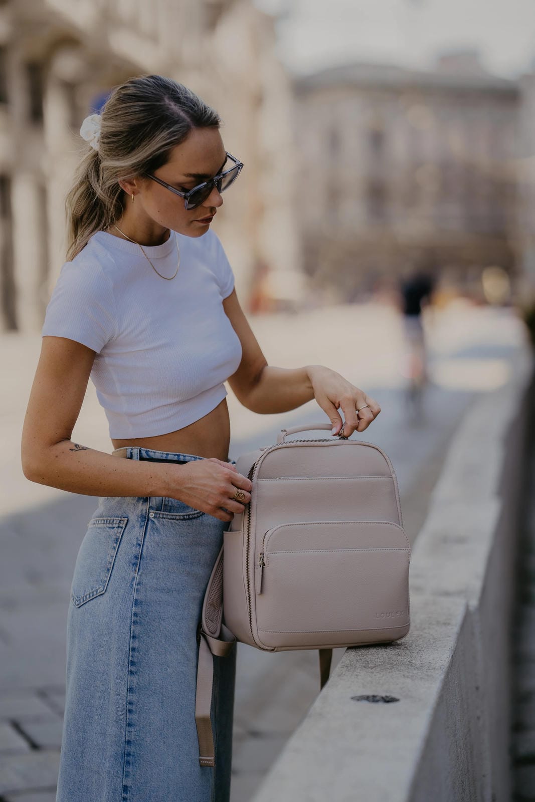 Woman holding a beige backpack on a city street