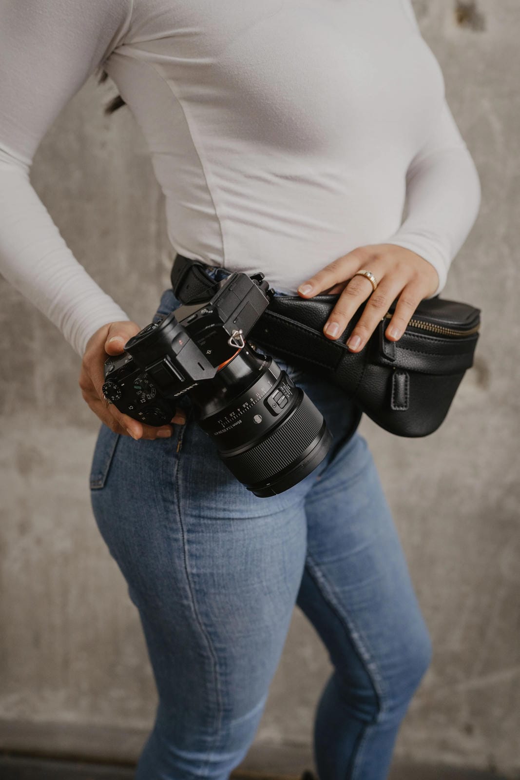 Person holding two camera bodies and a lens against a neutral background