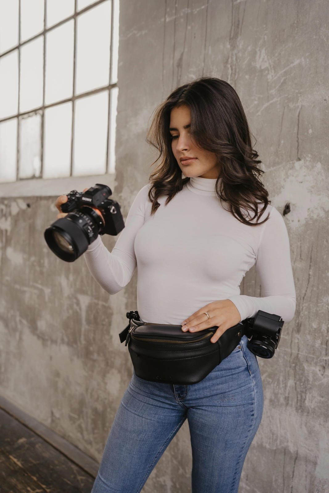 Woman holding a camera with a waist bag against a textured wall.