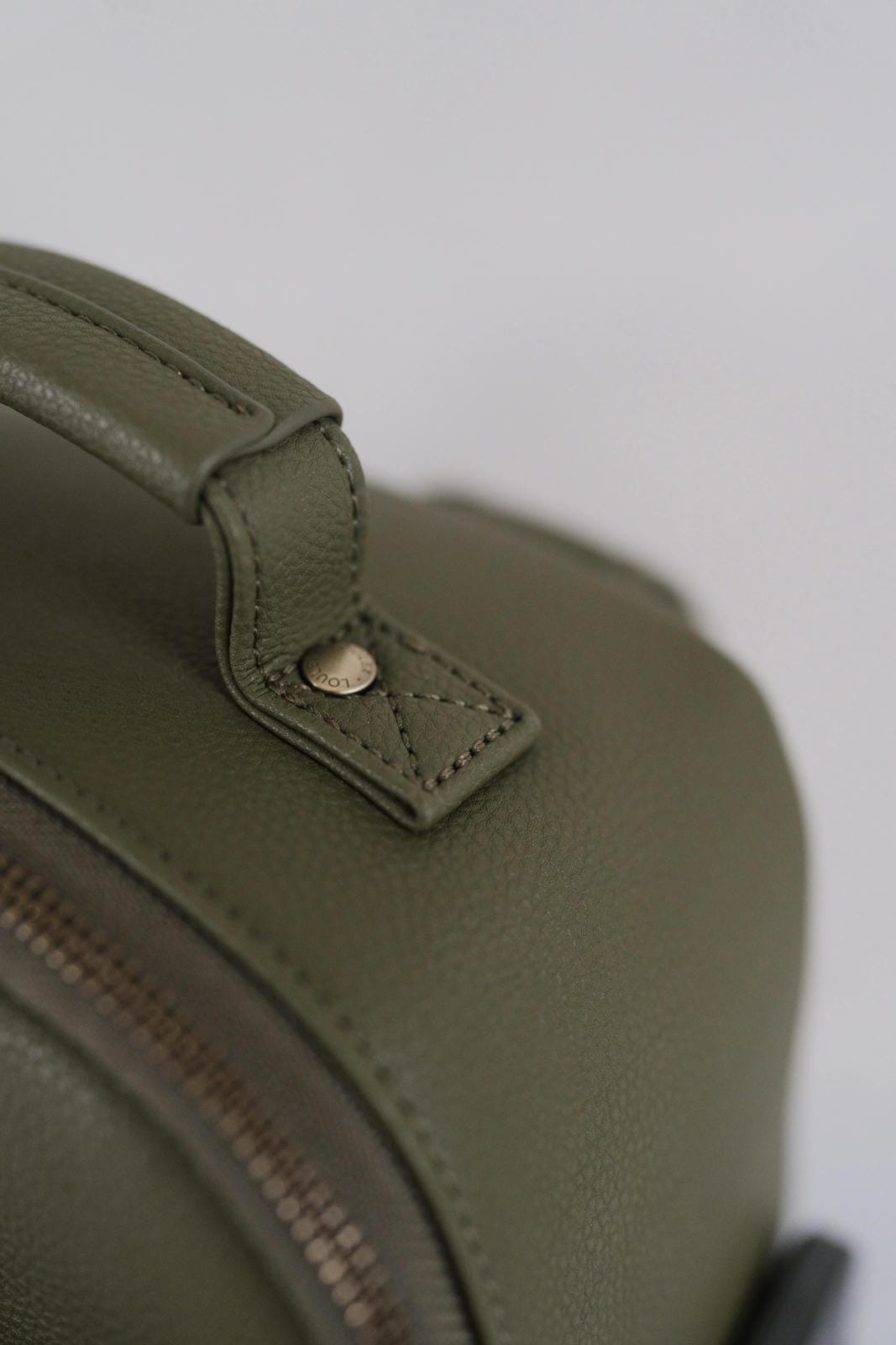 Close-up of a green leather bag with a visible brand logo on a white background