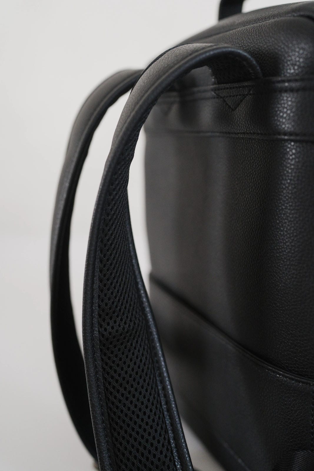 Close-up of a black leather backpack with a strap on a light gray background