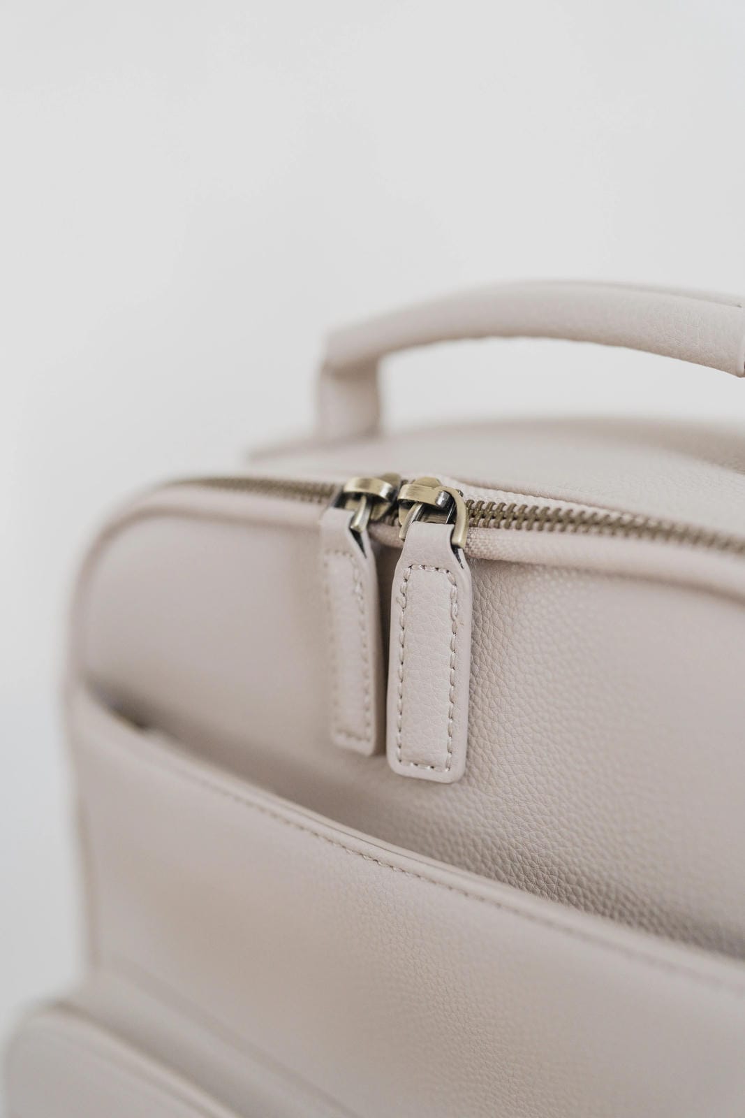 Close-up of a beige leather bag with a zipper on a light background