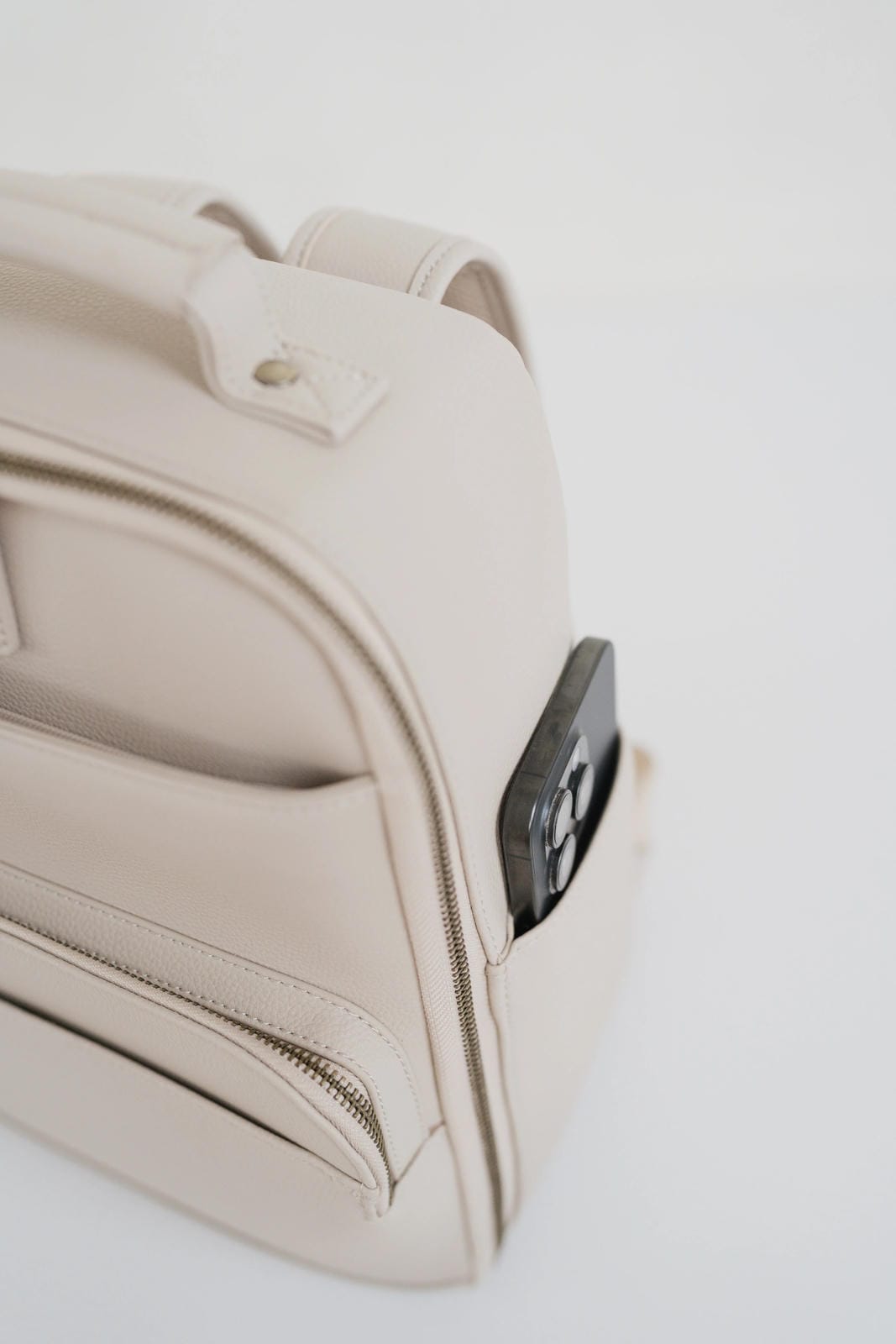 Beige backpack with a black zipper on a light gray background