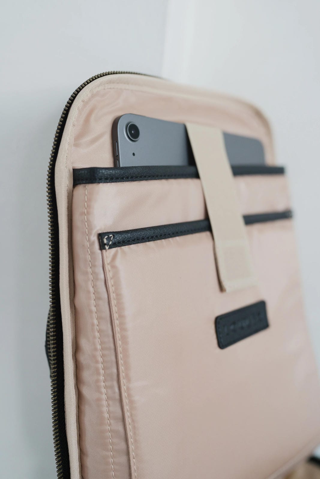 Beige pouch with black zippers and phone pocket on a light gray background