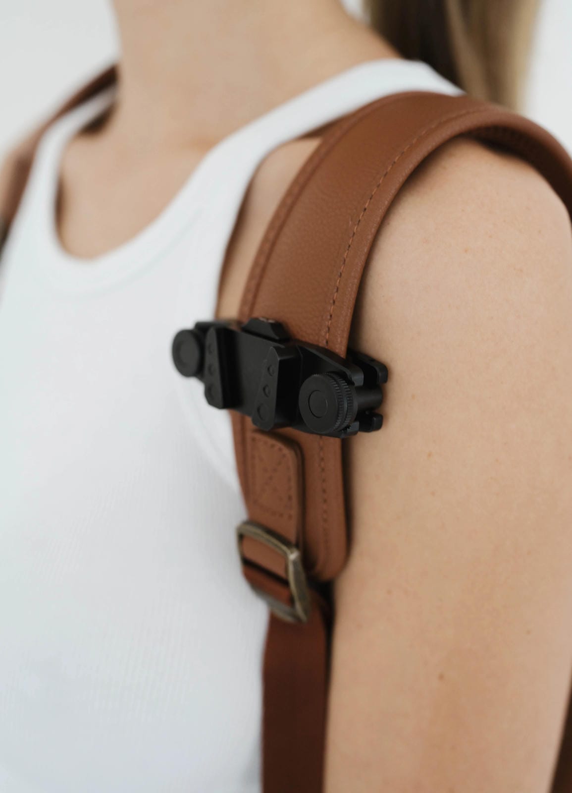 Brown leather strap with a black metal clip on a person wearing a white tank top.