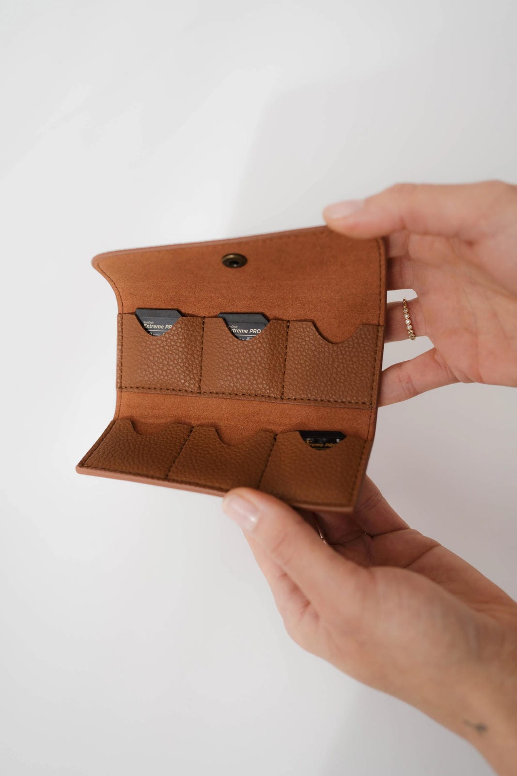 Brown leather wallet held by a hand against a white background