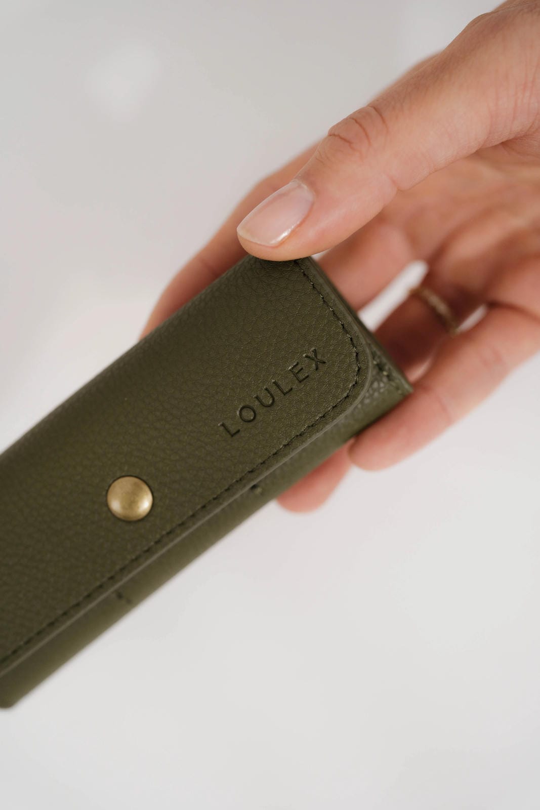 Green wallet with 'LOULEX' branding held by a hand on a light background