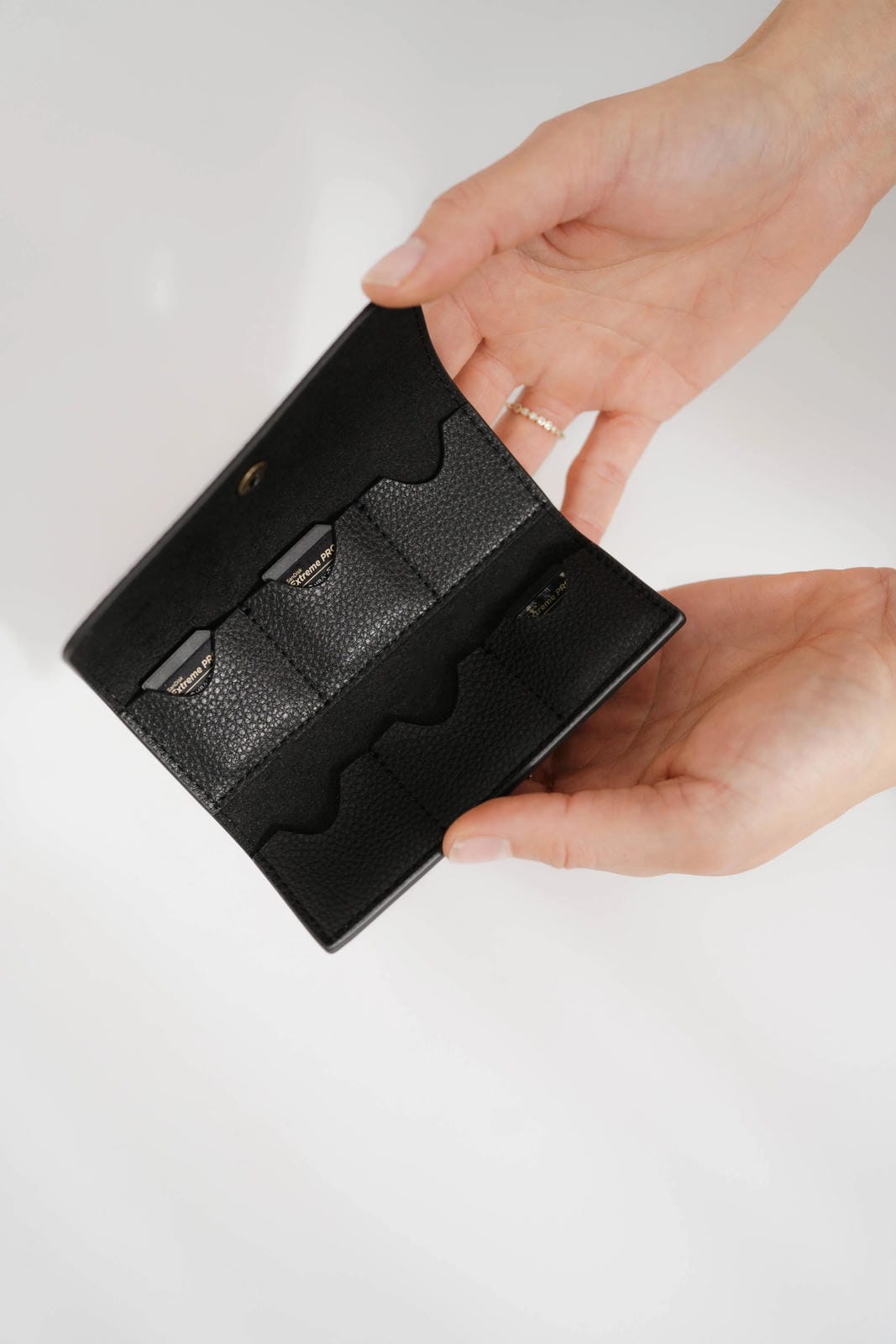 Black leather wallet held by a hand on a light gray background