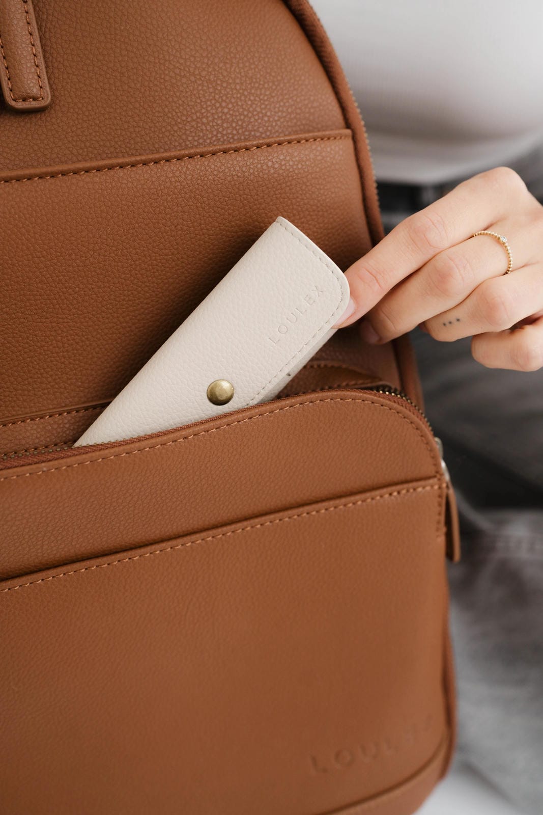 Brown leather backpack with a hand reaching in to place a white wallet inside.