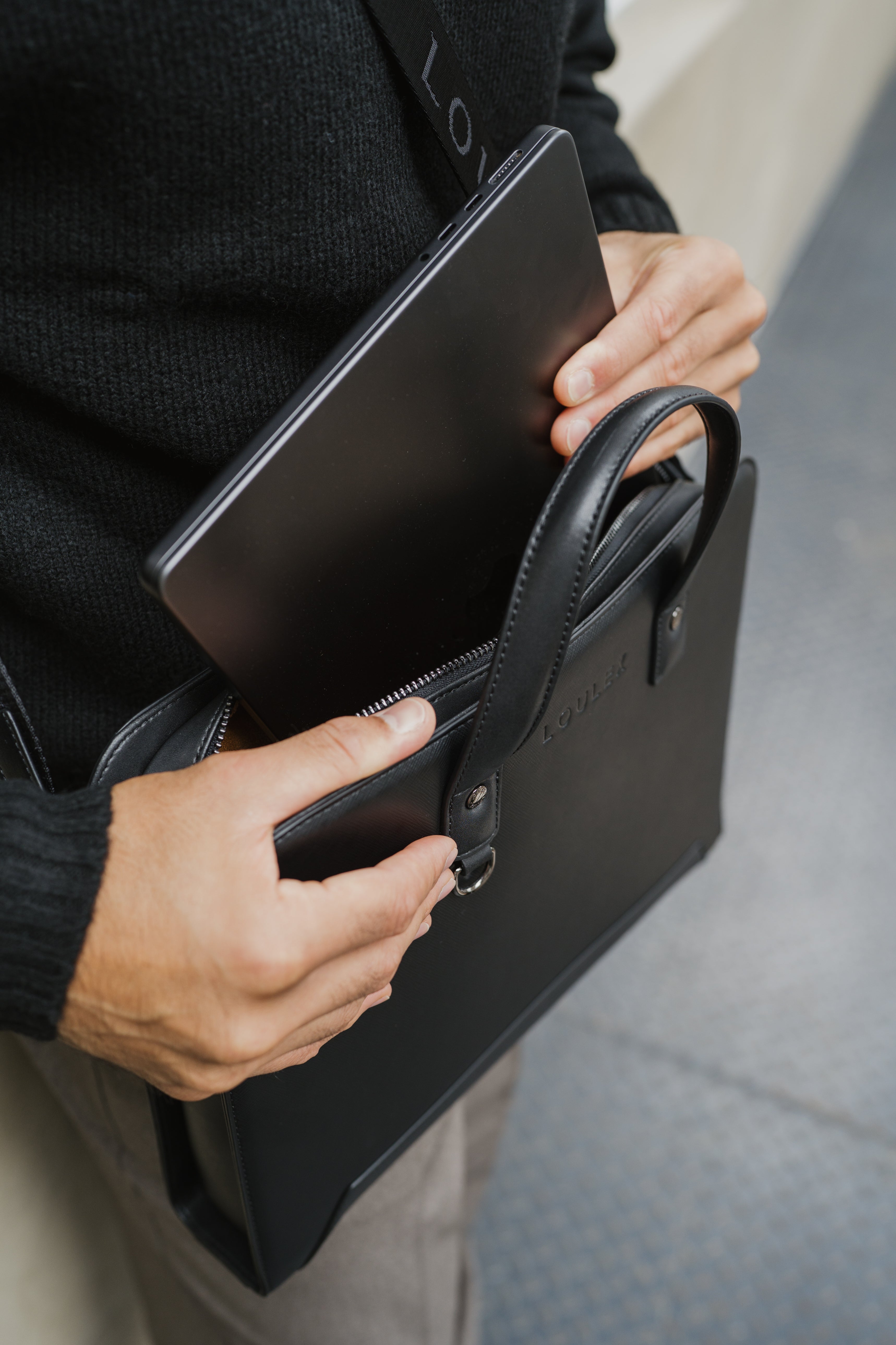 Person holding a black leather briefcase with a blurred background