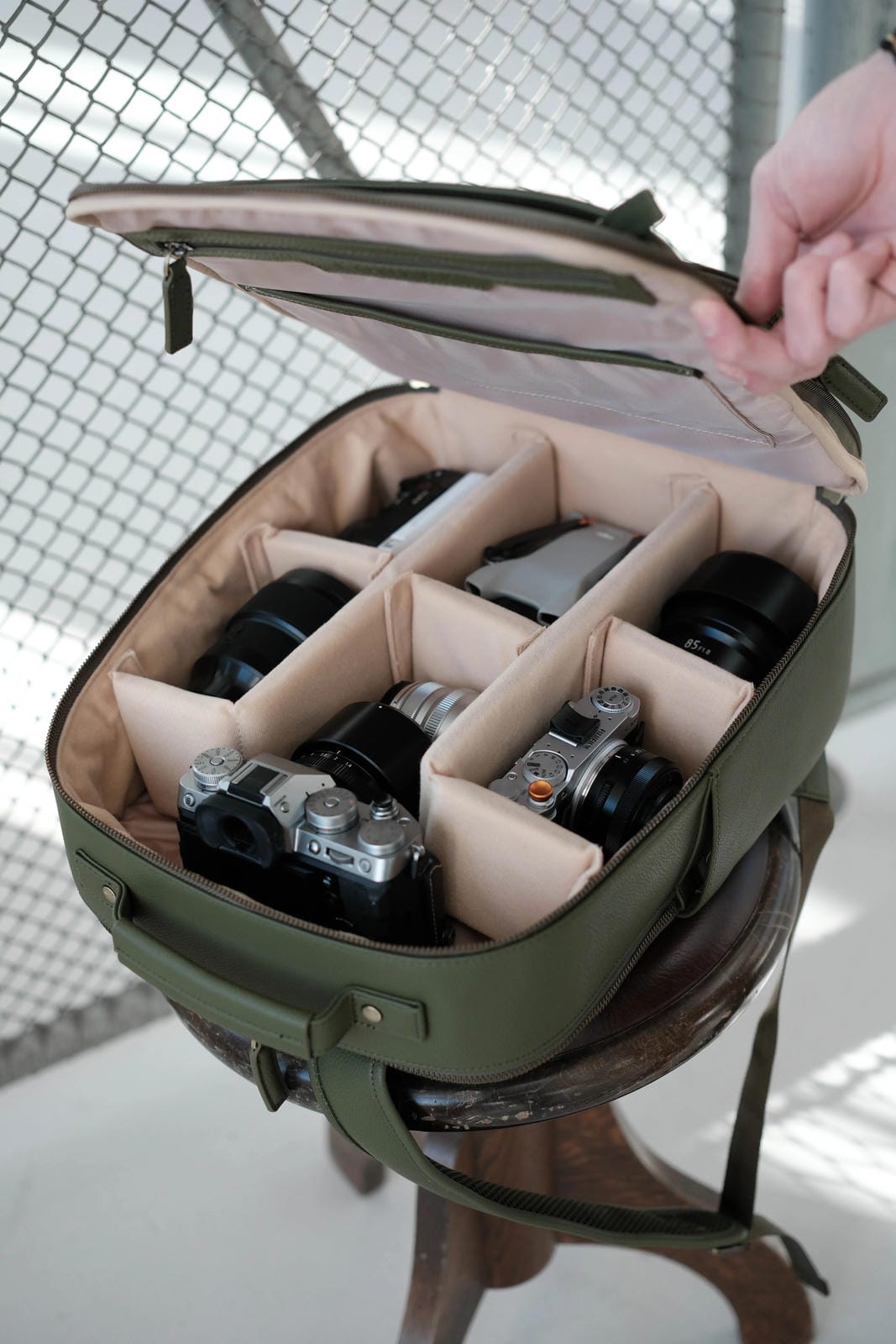 Green camera bag with compartments holding cameras on a stool outdoors.